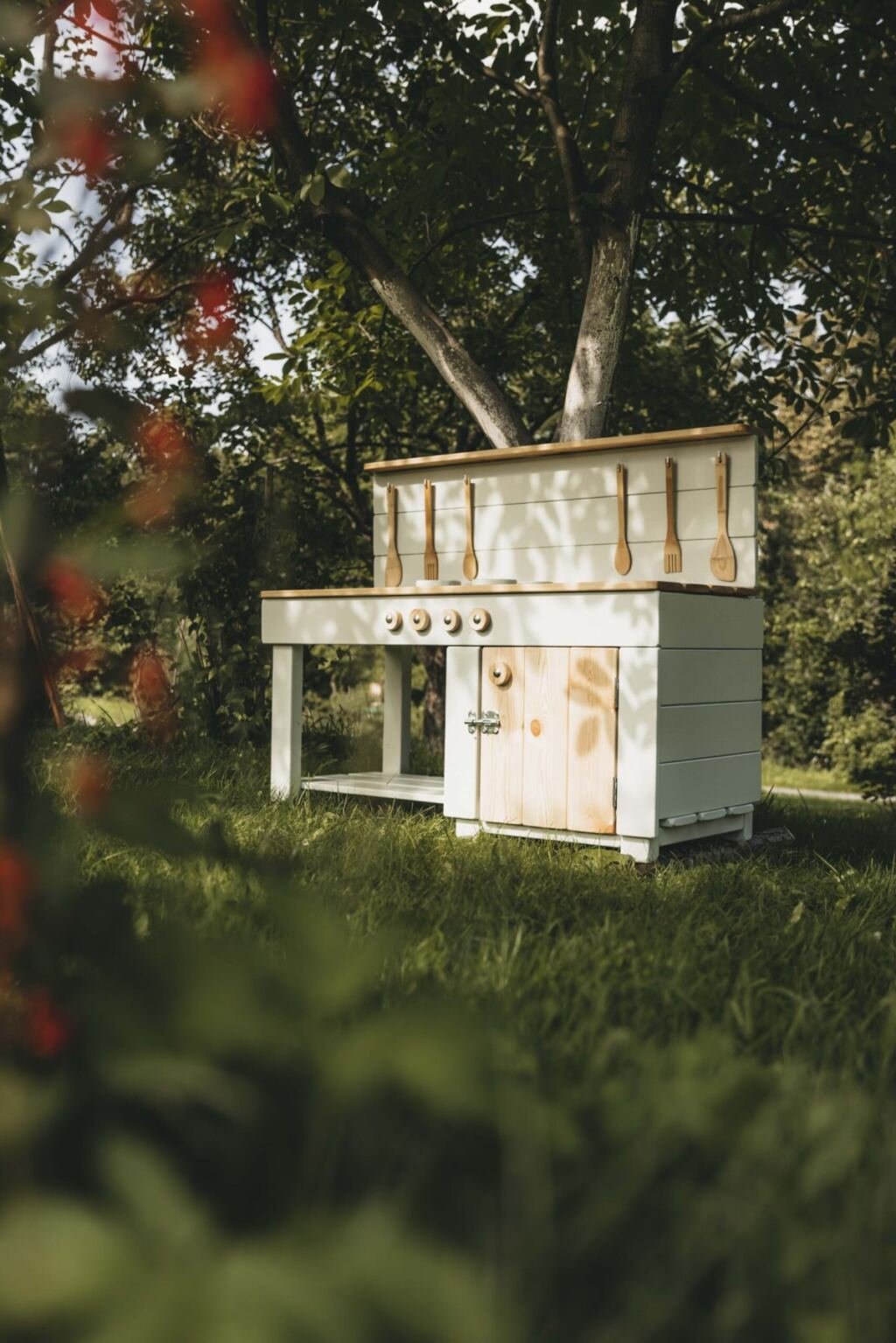 A finished wooden mud kitchen with a storage cabinet standing in a garden