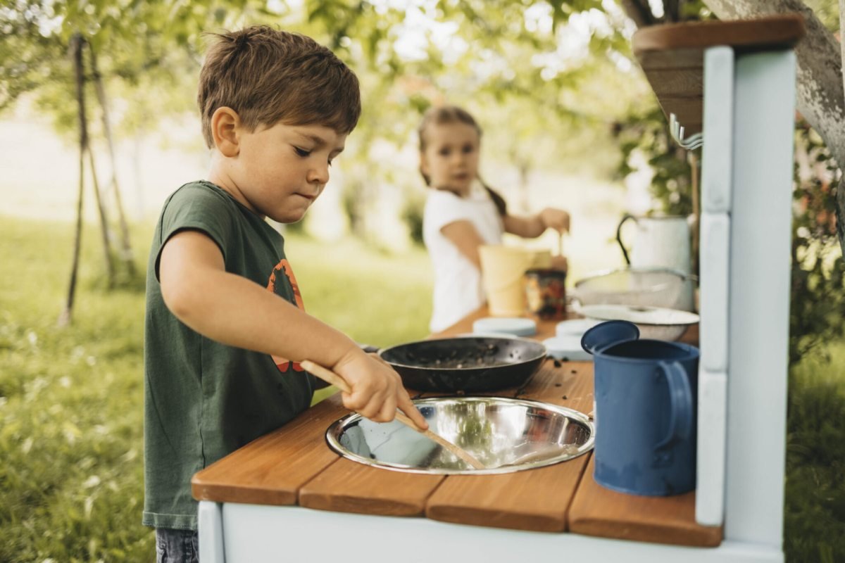 Children playing at a handcrafted wooden mud kitchen in a British garden