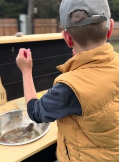 Children playing at a wooden mud kitchen in a real garden