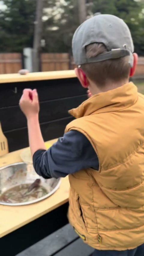 Children playing at a wooden mud kitchen in a real garden